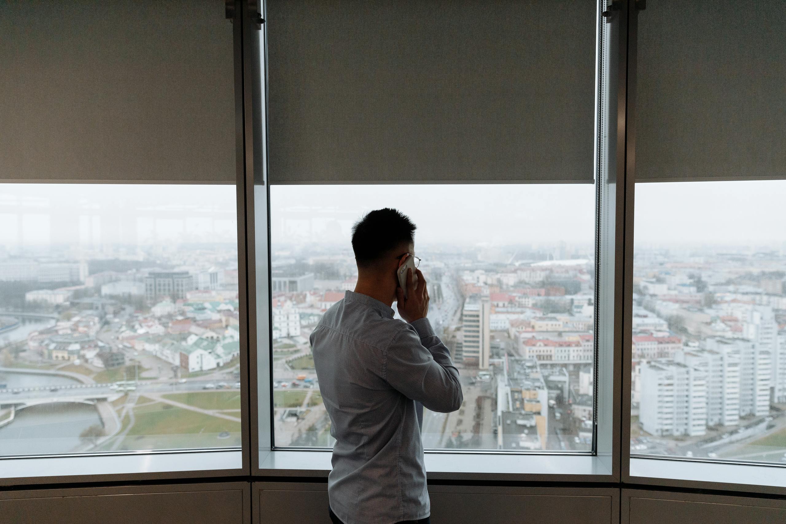 Businessman standing by window, making a phone call with city view.